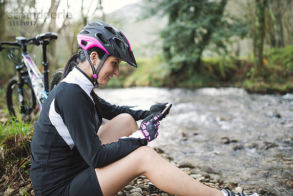 Lächelnde Frau mit Mountainbike in der Natur beim Handy-Check