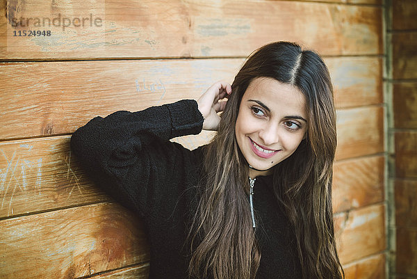 Porträt einer lächelnden jungen Frau vor einer Holzwand  die etwas beobachtet.