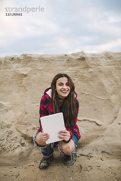 Porträt einer lächelnden jungen Frau mit am Strand kauernder Tafel