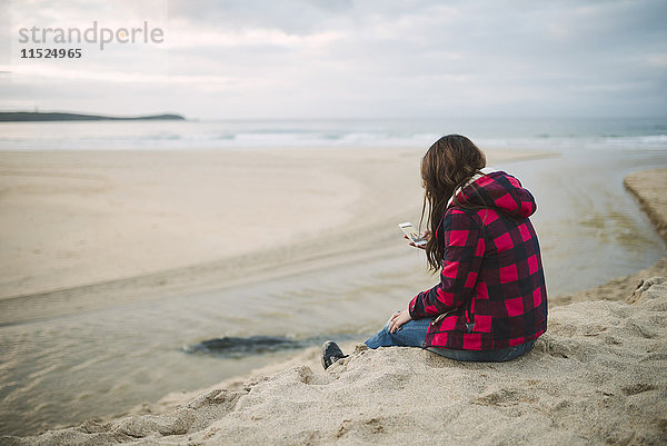 Junge Frau am Strand mit Blick auf das Handy