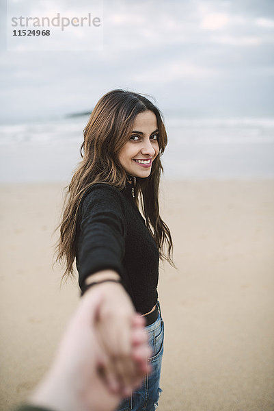 Porträt einer glücklichen jungen Frau  die am Strand die Hand hält