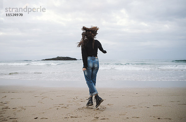 Rückansicht der jungen Frau beim Springen am Strand