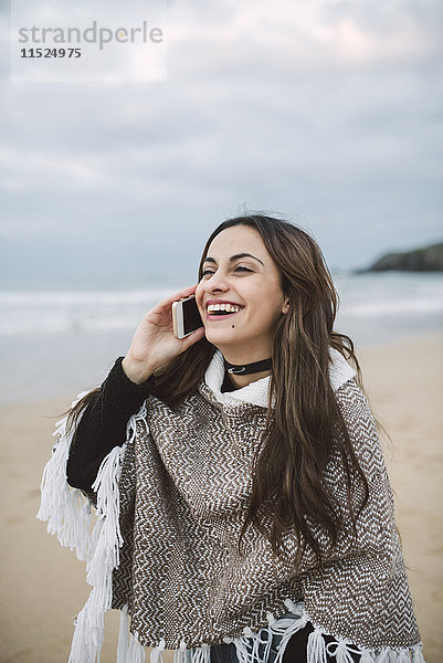 Porträt einer glücklichen jungen Frau am Telefon am Strand