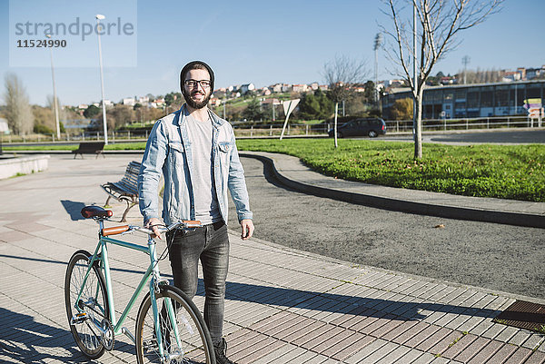 Junger Mann  der mit seinem Fixie Bike in einem Park spazieren geht.