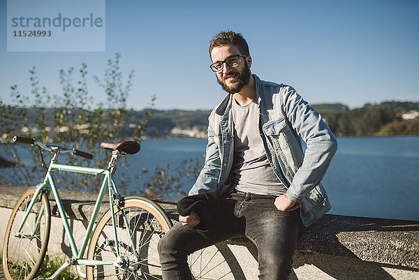 Lächelnder junger Mann mit seinem Fixie Bike am Wasser