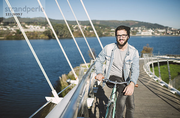 Lächelnder junger Mann mit seinem Fixie Bike auf einer Brücke