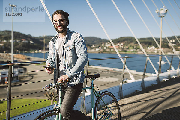 Lächelnder junger Mann mit Fixie Bike auf einer Brücke