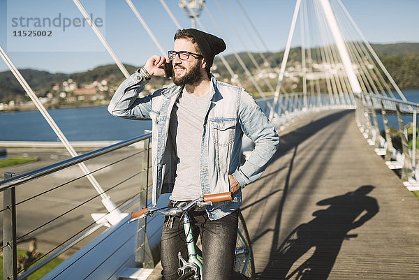 Junger Mann mit Fixie Bike auf einer Brücke am Telefon