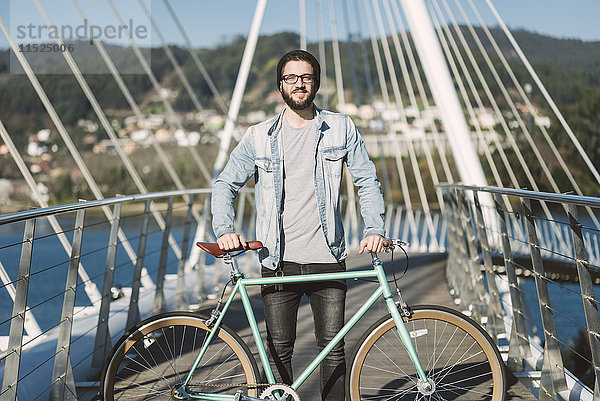 Lächelnder junger Mann mit seinem Fixie Bike auf einer Brücke