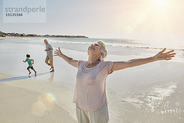 Fröhliche Seniorin mit ausgestreckten Armen am Strand stehend