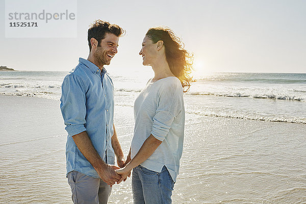 Ein glückliches Paar hält sich am Strand an den Händen.