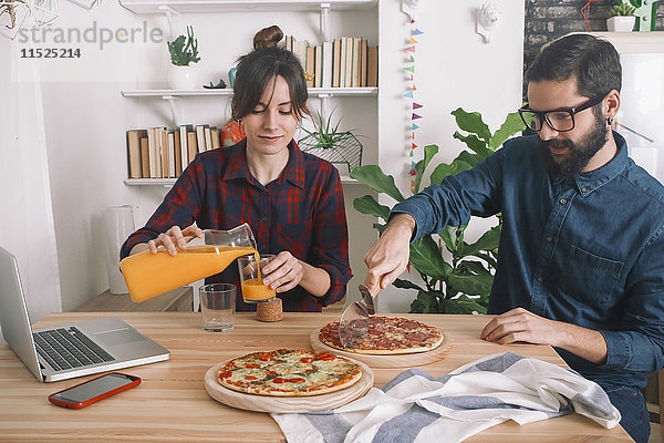 Junges Paar isst Pizza und trinkt Saft zum Mittagessen  Laptop steht auf dem Tisch