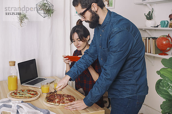 Junges Paar beim Pizzaessen und Safttrinken zum Mittagessen  Frau beim Fotografieren mit Smartphone