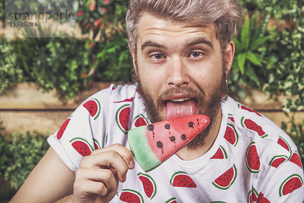 Porträt eines jungen Mannes  der Wassermelonen-Eis-Lolly auf der Terrasse isst.