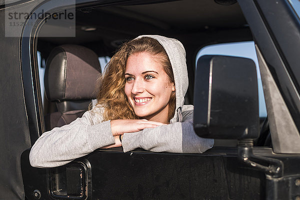 Porträt einer glücklichen jungen Frau  die sich aus dem Autofenster lehnt.