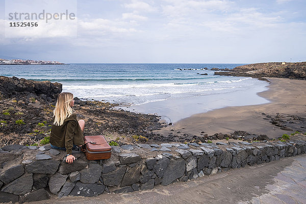 Spanien  Teneriffa  junge blonde Frau an der Wand am Strand sitzend