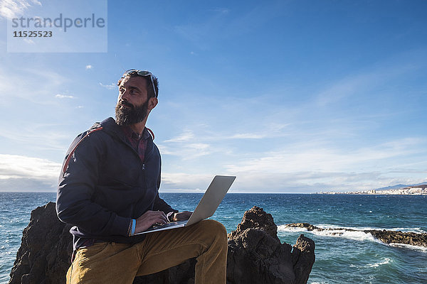 Spanien  Teneriffa  Portrait eines Mannes mit Laptop vor dem Meer