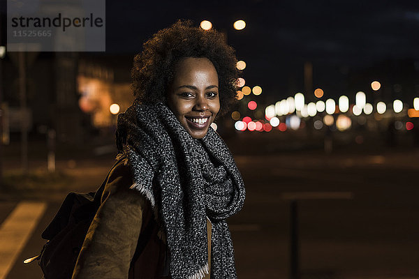 Porträt einer lächelnden jungen Frau am Straßenrand bei Nacht