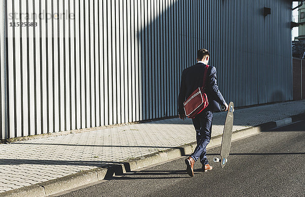 Junger Geschäftsmann auf der Straße mit Skateboard unterwegs