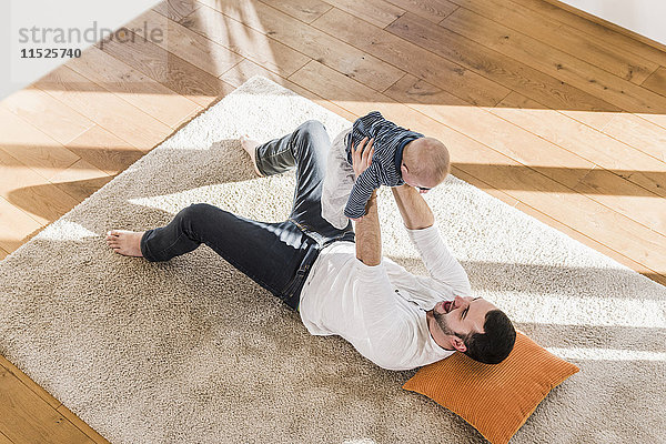 Vater spielt mit dem kleinen Sohn  auf dem Teppich liegend