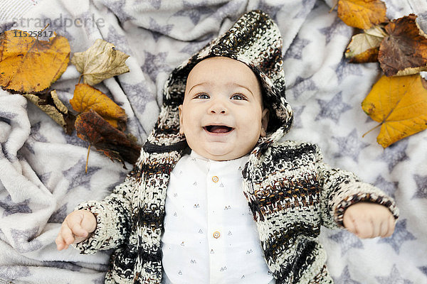 Fröhlicher Junge auf einer Decke mit Herbstblättern liegend