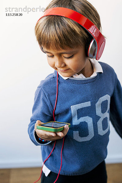 Kleiner Junge hört Musik mit Kopfhörern und schaut auf das Smartphone.
