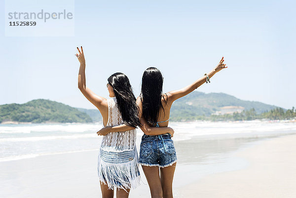 Brasilien  Sao Paulo  Ubatuba  zwei junge Frauen stehen Arm in Arm am Strand.