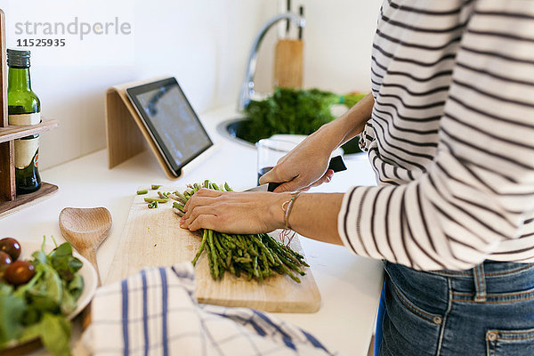 Junge Frau beim Kochen zu Hause mit digitaler Tablette für das Rezept