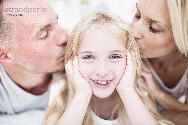 Porträt eines lächelnden Mädchens  das von den Eltern geküsst wird.