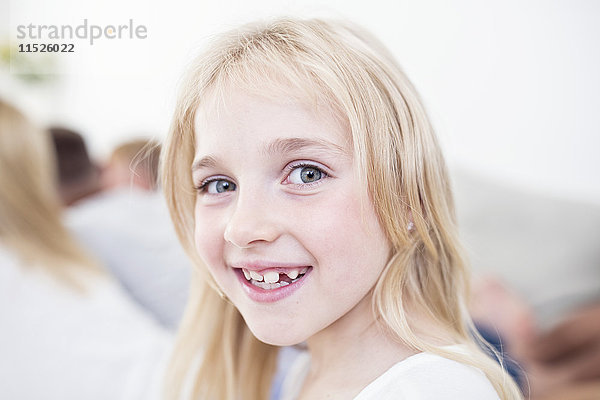 Porträt eines lächelnden blonden Mädchens mit Familie im Hintergrund