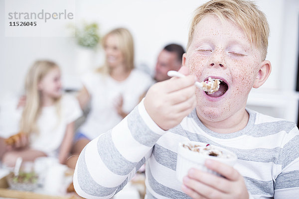 Junge isst aus Müslischale mit Familie im Hintergrund