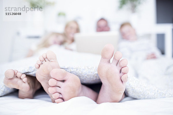 Füße der Familie im Bett liegend mit Laptop
