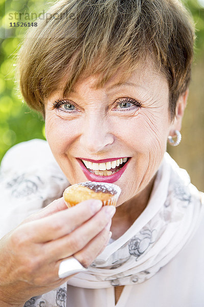 Porträt einer lächelnden älteren Frau  die einen Muffin im Freien isst.