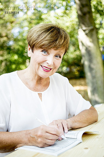 Porträt einer lächelnden Seniorin bei einem Kreuzworträtsel im Freien