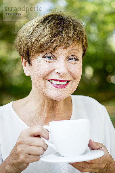 Porträt einer lächelnden Seniorin beim Kaffeetrinken im Freien