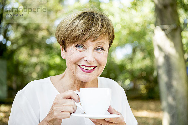 Porträt einer lächelnden Seniorin beim Kaffeetrinken im Freien