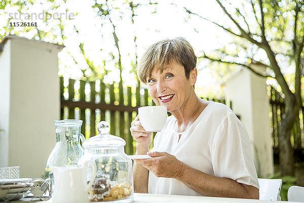 Porträt einer lächelnden Seniorin beim Kaffeetrinken im Freien