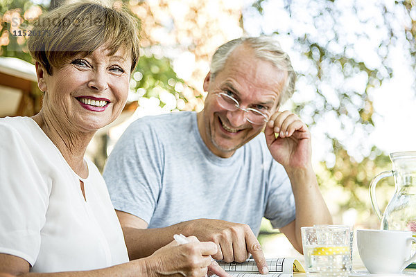 Lächelndes Seniorenpaar im Freien beim gemeinsamen Kreuzworträtselspiel