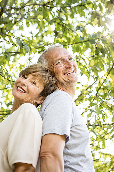 Porträt eines glücklichen älteren Paares Rücken an Rücken im Freien