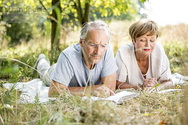 Seniorenpaar auf der Wiese liegend beim Lesen eines Buches