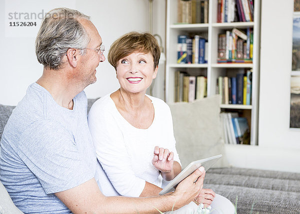 Seniorenpaar zu Hause auf der Couch sitzend mit digitalem Tablett