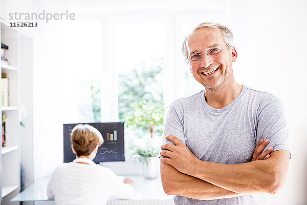 Porträt eines lächelnden älteren Mannes mit Frau im Hintergrund am Computer