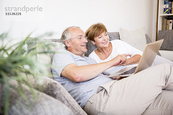 Seniorenpaar zu Hause sitzend auf der Couch mit Laptop