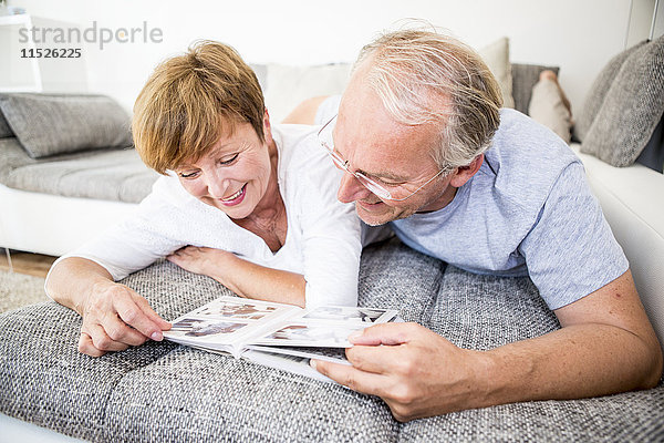Seniorenpaar zu Hause auf der Couch liegend beim Betrachten des Fotoalbums
