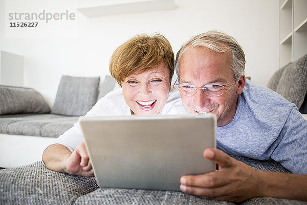 Glückliches Seniorenpaar zu Hause auf der Couch liegend mit digitalem Tablett
