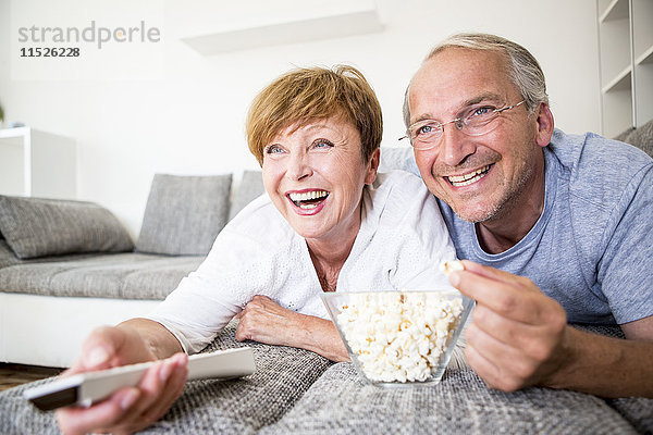 Glückliches älteres Paar zu Hause  das auf der Couch liegt und fernsieht.
