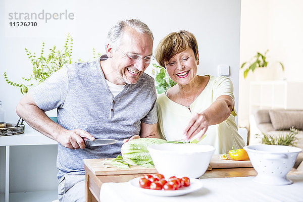 Fröhliches Seniorenpaar in der Küche beim gemeinsamen Salat zubereiten