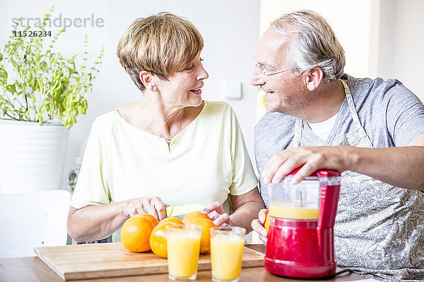 Seniorenpaar in der Küche bereitet frisch gepressten Orangensaft zu.