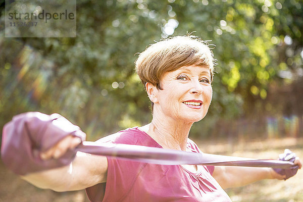 Porträt einer lächelnden Seniorin beim Training mit Widerstandsband im Freien