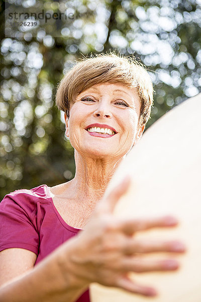 Porträt einer lächelnden Seniorin mit Fitnessball im Freien